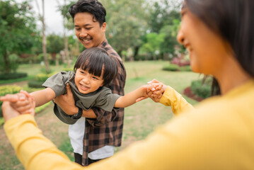 beautiful woman holds both hands of a boy while being carry as if flying by a man outdoors