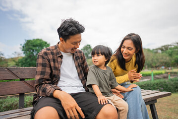 father, mother and little boy sitting chatting on a park bench