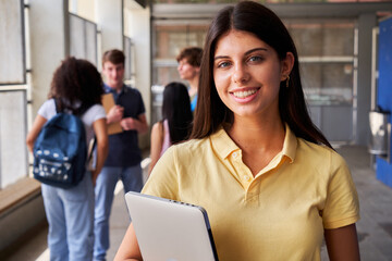 Cheerful portrait of a brunette female high school student looking at camera smiling holding notebooks after class. Copy space image.