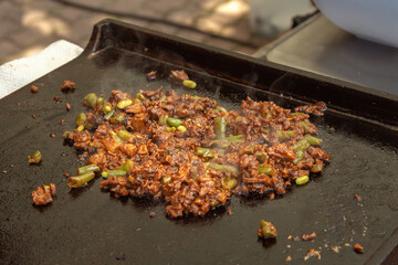 Pieces of meat with onions and vegetables are fried on a metal sheet as a filling for pita bread, sandwich or burrito. Street food. Fast food. Close-up