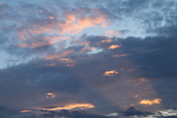 The evening sky is filled with warm shades of orange and pink as the sun begins to set. Bright rays of light pierce through the clouds, creating a striking contrast with the darker parts of the sky.

