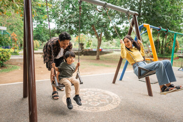 little boy with dad on the swing and mom playing in the park