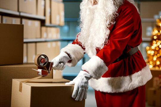 Santa Claus taping a delivery box at the warehouse - Powered by Adobe
