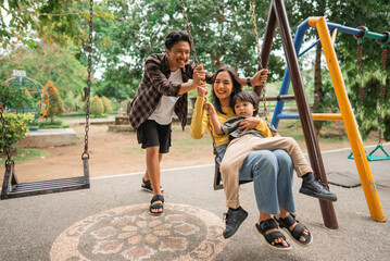dad pushes the swing while mom holds little boy on her lap while playing on the swing in the park