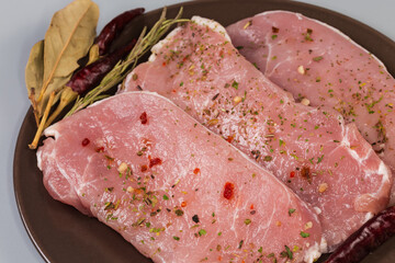 Raw boneless pork chops with spices on dish, close-up