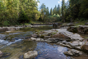 Mountain river section with narrow wooden footbridge at autumn day