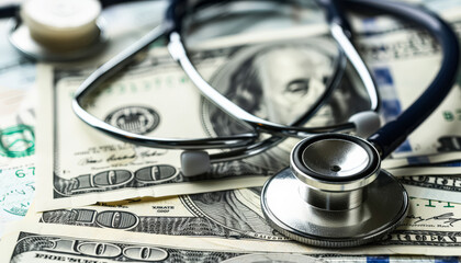 Stethoscope is on top of a stack of money. The stethoscope is silver and the money is green