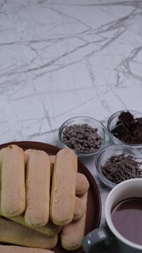 Video verticale, piatto con biscotti , tazza di cioccolata e ciotole con cioccolata in pezzi, fave di cioccolato sul tavolo