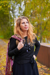 Beautiful woman in black dress and necklace walking in autumn forest. Relaxation concept