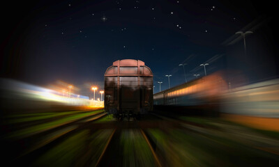 Freight wagon on the siding with transport goods and passing goods trains at night at the station.