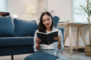 Young woman is smiling while reading a book in her living room, enjoying a quiet moment of relaxation