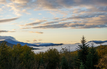 Sunrise over a fog covered forest and mountains in background