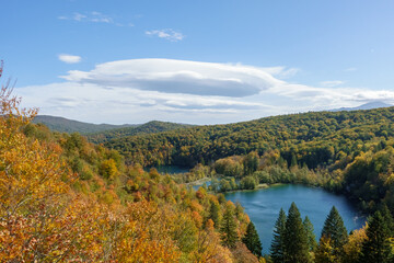 View over an autumn colored forest with a blue mountain lake against blue sky with fair weather clouds