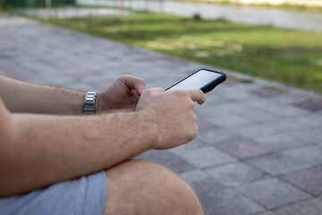 Man using Smartphone while Sitting Outdoor on a Bench. 