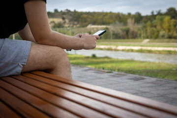 Man using Smartphone while Sitting Outdoor on a Bench. 