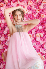 A woman in a pink dress poses for a photo. She is wearing a necklace and earrings. The pink background and the woman's outfit create a romantic and elegant mood.