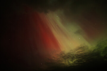 A vivid display of the Aurora Borealis lights up the night sky, with striking red, orange, and green hues blending amidst dark clouds. The dramatic contrast creates a surreal and captivating scene.