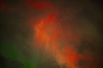 A captivating scene of the Aurora Borealis with vibrant red and orange hues illuminating the night sky. Dark clouds add drama, while subtle green light emerges through the atmosphere