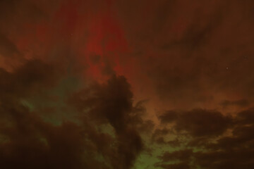 A captivating scene of the Aurora Borealis with vibrant red and orange hues illuminating the night sky. Dark clouds add drama, while subtle green light emerges through the atmosphere