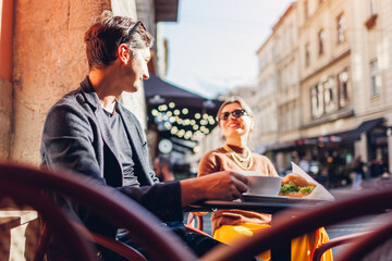 Young couple in love relaxing in outdoor cafe drinking coffee eating croissants on Lviv city street in Europe