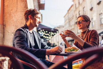 Young couple in love relaxing in outdoor cafe drinking coffee eating croissants on Lviv city street in Europe