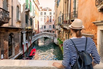 Elegant woman with hat enjoys the view on a canal with passing gondola in Venice, Italy © xamnex