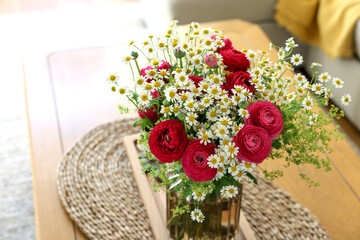 Beautiful ranunculus flowers and chamomiles in vase on table indoors