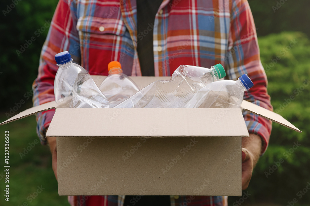 Wall mural Recycling. Man holding cardboard box with plastic bottles outdoors, closeup