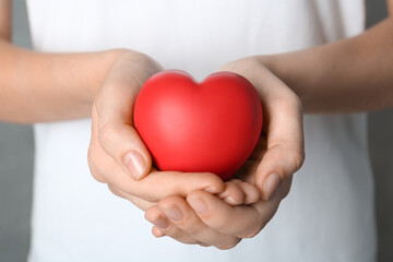 Woman holding red heart on grey background, closeup