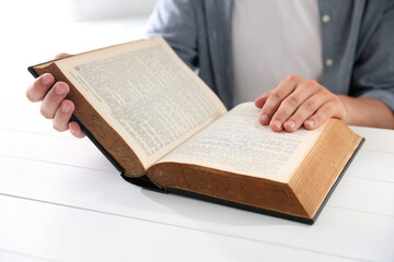 Naklejka premium Man with Bible at white wooden table, closeup