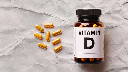 Bottle of Vitamin D capsules on a textured surface with scattered pills.