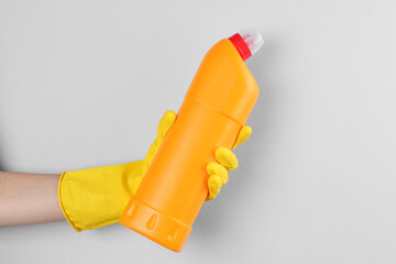 Woman holding toilet cleaner in bottle on light background, closeup