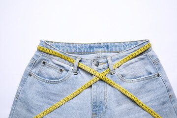 Jeans and measuring tape on white background, top view