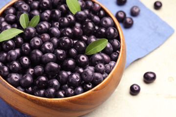 Ripe acai berries and leaves in bowl on grey table, closeup