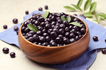Ripe acai berries and leaves in bowl on grey table, closeup