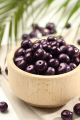 Ripe acai berries in bowl on light table, closeup