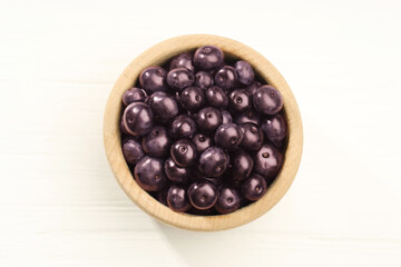 Ripe acai berries in bowl on white wooden table, top view