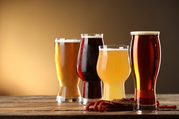 Glasses with different types of beer and snacks on wooden table against color background