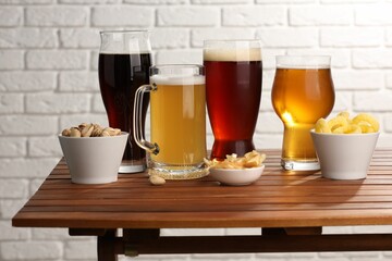 Glasses with different types of beer and snacks on wooden table against white brick wall