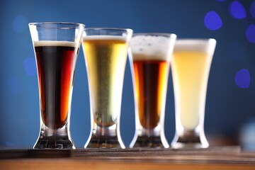 Glasses with different types of beer on wooden table against blue background, closeup