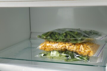 Plastic bags with different frozen vegetables in refrigerator, closeup