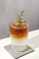 Refreshing espresso tonic drink with rosemary on white table