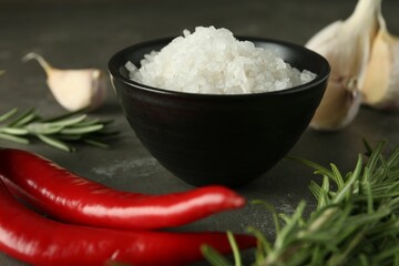Sea salt in bowl, rosemary, chili peppers and garlic on grey table, closeup