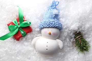 Cute decorative snowman, fir tree branches and gift box on artificial snow, flat lay
