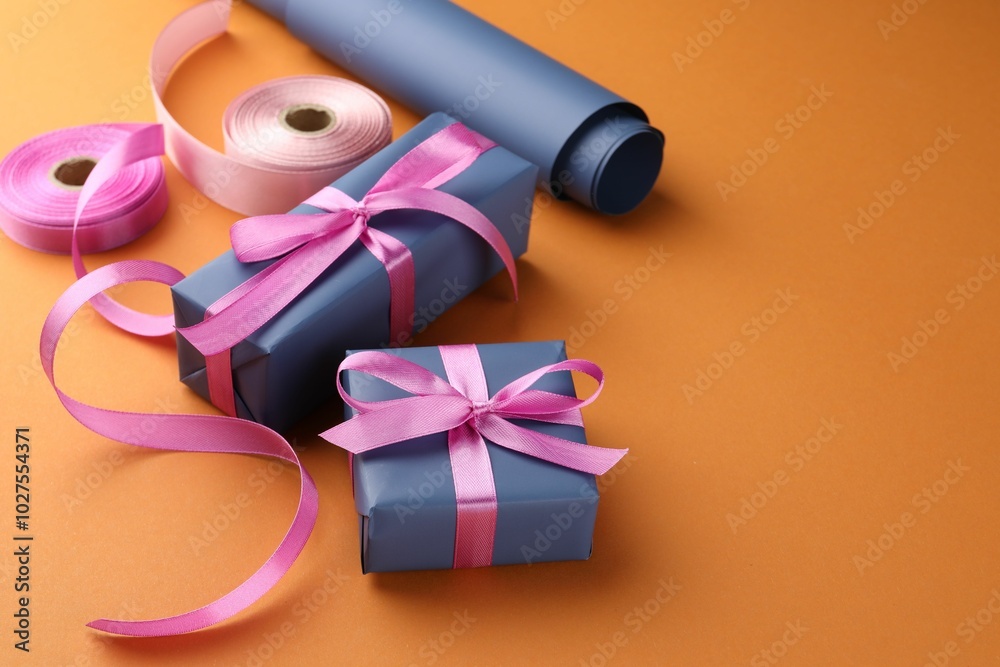 Sticker Beautiful gift boxes with pink bows, ribbons and roll of wrapping paper on orange background, space for text