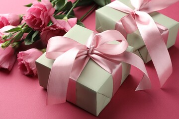 Beautiful gift boxes with bows and eustoma flowers on pink background, closeup