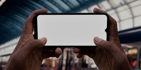 Black African-American old male using smartphone with a blank white screen. Train, station, platform apps mockup. Horizontal phone orientation