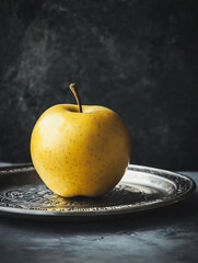 A golden apple sits on an engraved silver plate. 