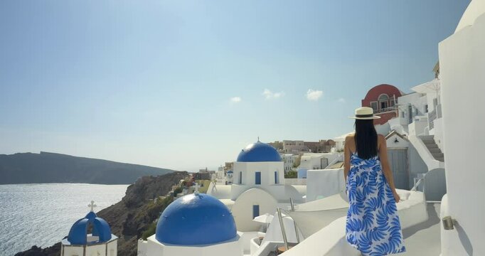 Attractive woman walking near iconic white buildings and blue dome churches in Santorini, Greece. Slow motion