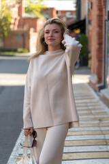 Obraz premium Portrait of beautiful smiling long haired caucasian blond woman in blank white sweater standing outdoor on city street in a sunny day on zebra crossing. Soft focus. Beautiful people and fashion theme